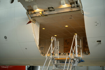 Open airplane cargo hold with stairs leading to the interior loaded with boxes.