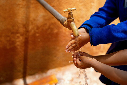 Two children washing hands under a water tap outdoors on a sunny day. Tanzania, Africa