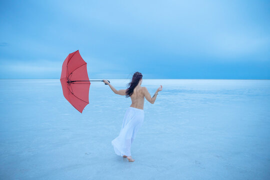 Woman holding a red umbrella stands on a vast, serene salt flat under a blue sky. Bonneville Salt Flats, Utah, USA