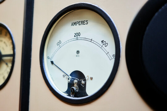 Close-up of an analog ammeter with needle pointing at zero amperes on a beige panel.