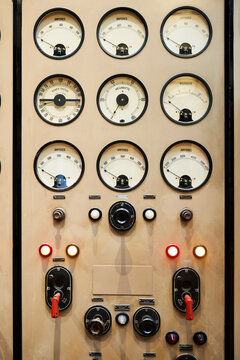 Vintage control panel with dials, gauges, switches, and warning lights in sepia tones.
