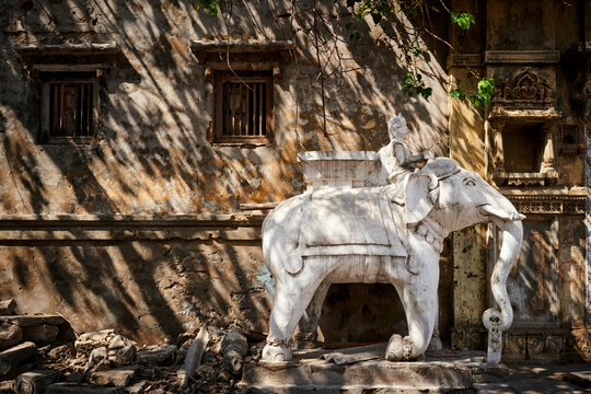 Stone elephant statue with rider against an aged, dappled wall under tree shadows.