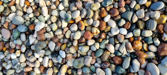 Macro image of wet, multicolored beach stones showing diverse textures and natural tones. Ideal for...