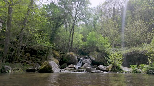 Small waterfall cascades over moss-covered rocks into a clear levada at Levadas de Jugueiros, surrounded by lush trees under a soft, natural light.