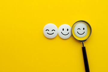 Magnifying glass focusing on a smiling face among neutral and sad emoticons, symbolizing positivity, happiness, and emotional choice on a vibrant yellow background.
