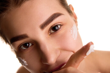 Extremely close up of young brunette woman with skin care cream on cheeks, looking at camera...
