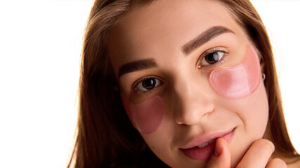 Close up photo of pretty young female model with well-groomed eyebrows, applying under eye hydrogel patches against white background. Concept of youth and natural beauty, cosmetology treatment. Ad