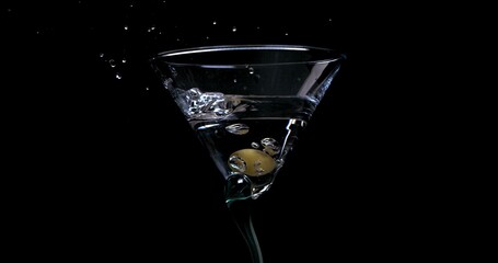 Olive falling into a glass with martini on a black background in slow motion