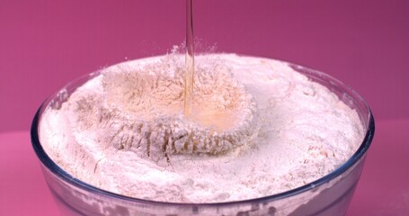 Egg falls into a bowl of flour in slow motion on a pink background