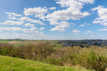 Fototapeta premium Overview of Maastricht, Terrain of hilly countryside green grass meadow and farmland, Combination with old and new modern buildings, Houses and church on hillside with blue sky, Limburg, Netherlands.
