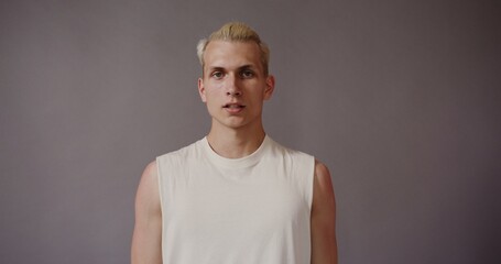 A blond young European with a stylish hairstyle, dressed in a white T-shirt, looks seriously at the...
