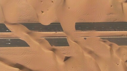 Aerial view of desert paved road buried by sand dunes. Dubai, United Arab Emirates. Daylight drone...