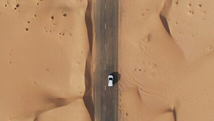 Vertical panning from a quadcopter. A white car is driving alone on a road in the desert. Aerial view of desert © m-art