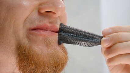 Man Pulling Off Black Hostage Tape from Lips Showing Sticky Texture Close-Up, Product Use Concept...