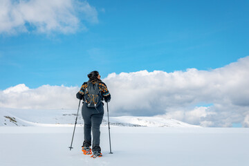 Woman snowshoeing across pristine snowy plains in Sierra de Gredos, Spain, with trekking poles and...