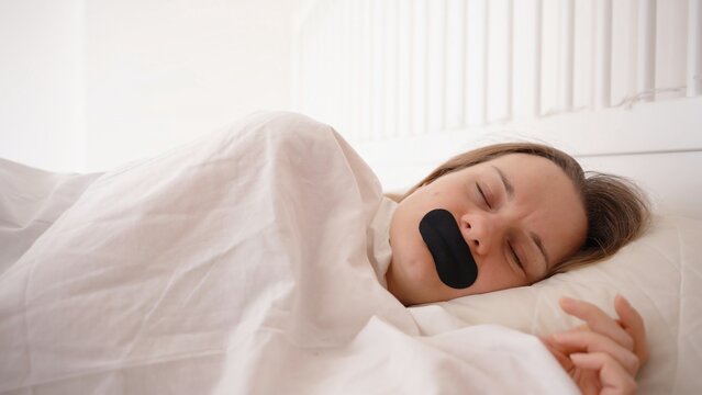 Woman Sleeping on Side Under White Blanket with Black Mouth Tape in Bright Bedroom, Silent Nighttime Nose Breathing Concept
