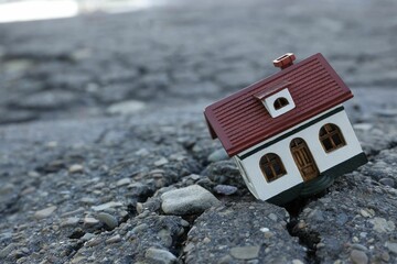 House model in cracked asphalt demonstrating earthquake disaster