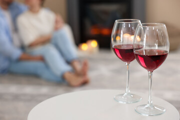 Couple near fireplace at home, focus on glasses of wine