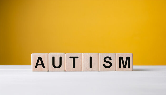 Wooden cubes with word AUTISM on table against yellow wall background.