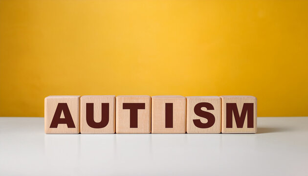 Wooden cubes with word AUTISM on table against yellow wall background.