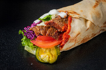 A delicious wrap containing seasoned meats, fresh vegetables, and sauces served on a warm tortilla