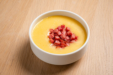 A creamy soup with vibrant diced meat, invitingly served on a wooden table