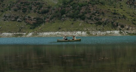 Russia, Caucasus. A guy photographs a girl with a camera, sitting in a rowing boat, opposite each other, in the middle of the lake against the backdrop of mountains covered with greenery. © m-art