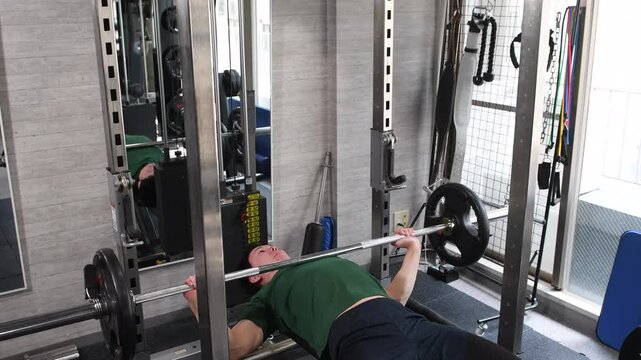 スポーツジムでベンチプレスをする若い男性