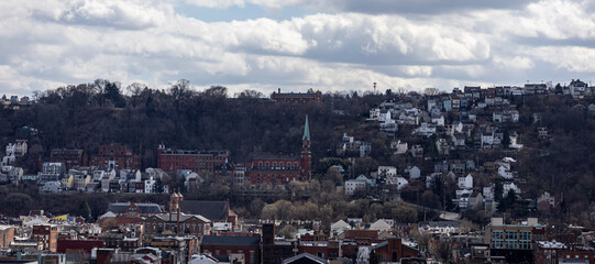 Pittsburgh, Pennsylvania, USA &ndash; March 18, 2024: A hillside view of Pittsburgh&rsquo;s South Side Slopes with dense residential homes and a church steeple under a cloudy afternoon sky.