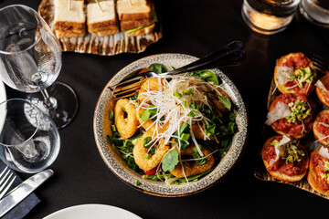 A plate of food with a salad and a bowl of fried food. The table is set with a wine glass and a fork