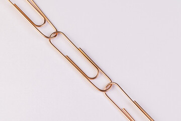 paper clips made of metal for the systematization, large sized copper paper clips lie on white blank paper closeup, top view