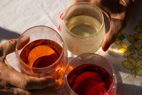 vista dettagliata di tre bicchieri pieni, su un tavolo, di cui due tenuti in mano da due persone, mentre fanno un brindisi con bevande diverse