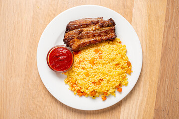 Succulent grilled meat rests on a bed of vibrant couscous with a flavorful sauce on the side