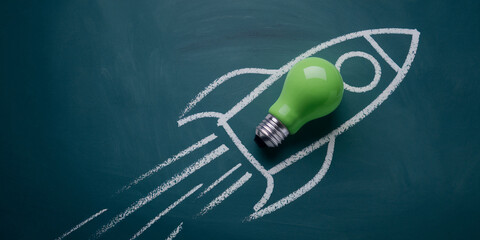 Green lightbulb atop a chalk rocket on a dark-green board, symbolizing innovative takeoff, new beginnings, and successful launch of ideas or projects Free space for text