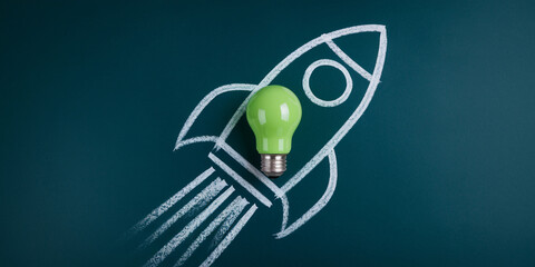 Green lightbulb atop a chalk rocket drawing on a dark-green chalkboard, symbolizing innovative ideas launching a new project or business Startup
