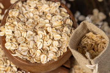 one bowl and a linen bag with oatmeal flakes for making porridge, scattered dry cereal flakes from oats, flattened, steamed and dried, close up