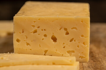 cheese with holes in place of slicing for cooking, pieces of sliced cheese on a cutting board, close up, side view