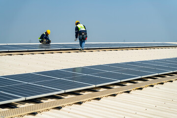 Fototapeta premium Two engineers install solar panels on a rooftop, wearing safety gear and helmets. The scene showcases renewable energy, green technology, and sustainable solutions under a clear blue sky.