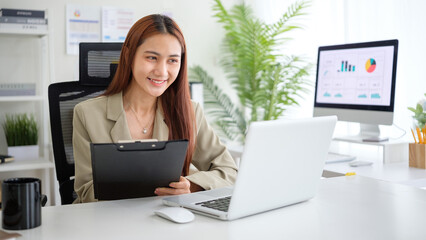 Smiling youn businesswoman working on a laptop in a bright, modern office.