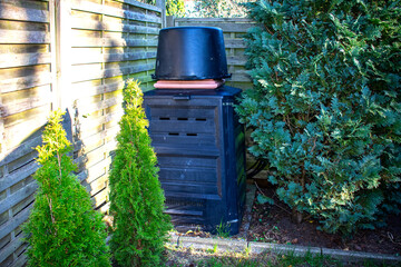 Compost container. A compost container stands in the corner near the fence in the garden. Thujas grow nearby. A garden in early spring on a sunny day. Nature. A container for plants.