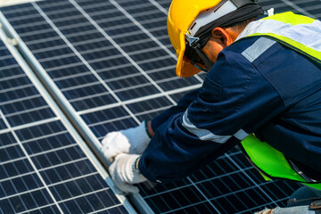 Two engineers install solar panels on a rooftop, wearing safety gear and helmets. The scene...