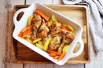Roasted chicken drumsticks with potatoes and carrots. Chicken legs grilled on a grill pan close-up. Horizontal view from above