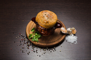 A pot with baked meat and a bread lid on a wooden stand