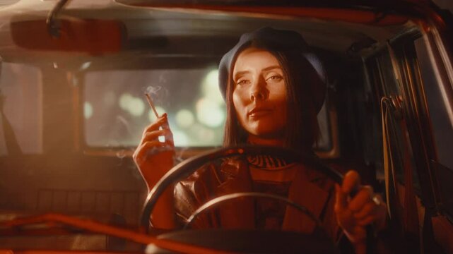 Young stylish female driver in elegant beret and leather jacket smoking cigarette during night ride in vintage car, with city street lights in background