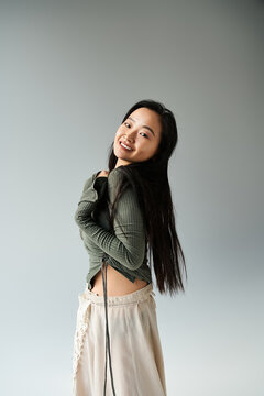 Young asian woman gracefully posing in stylish outfit against a soft gray backdrop