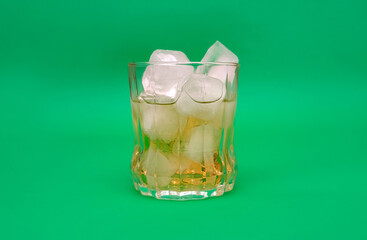 Glass of whiskey on green background. The clarity of the glass and the golden hue of the whiskey create an appealing visual.