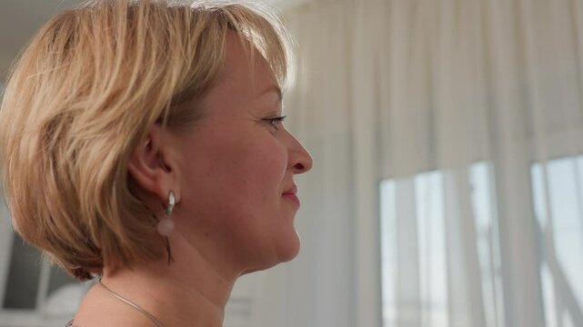 Close up of woman bringing rubber-like transparent soluble substance close to her nose to scent it with soft natural light filtering through sheer curtains in background,