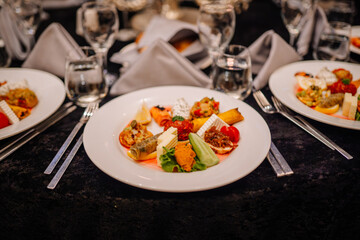 Gourmet appetizer plate with assorted vegetables, cheese, and dips on a banquet table with elegant tableware and folded napkins..