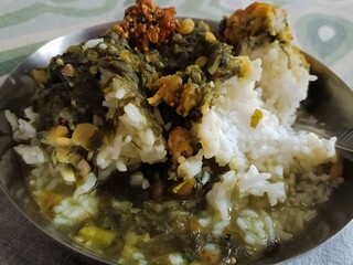 A comforting plate of steamed rice topped with dal saggā—slow-cooked spinach and chana dal—served with a side of spicy achar. A wholesome, rustic, and nourishing traditional meal.