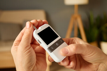 A person operates a sleek health monitoring device, focusing on its screen while seated in a comfortable living room filled with natural light